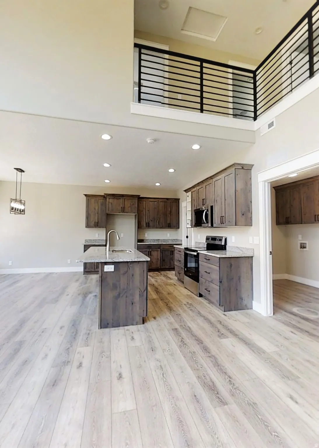 Kitchen featuring stainless steel appliances, dark wood finish cabinets, a high ceiling, light wood-style flooring, and a kitchen island with sink