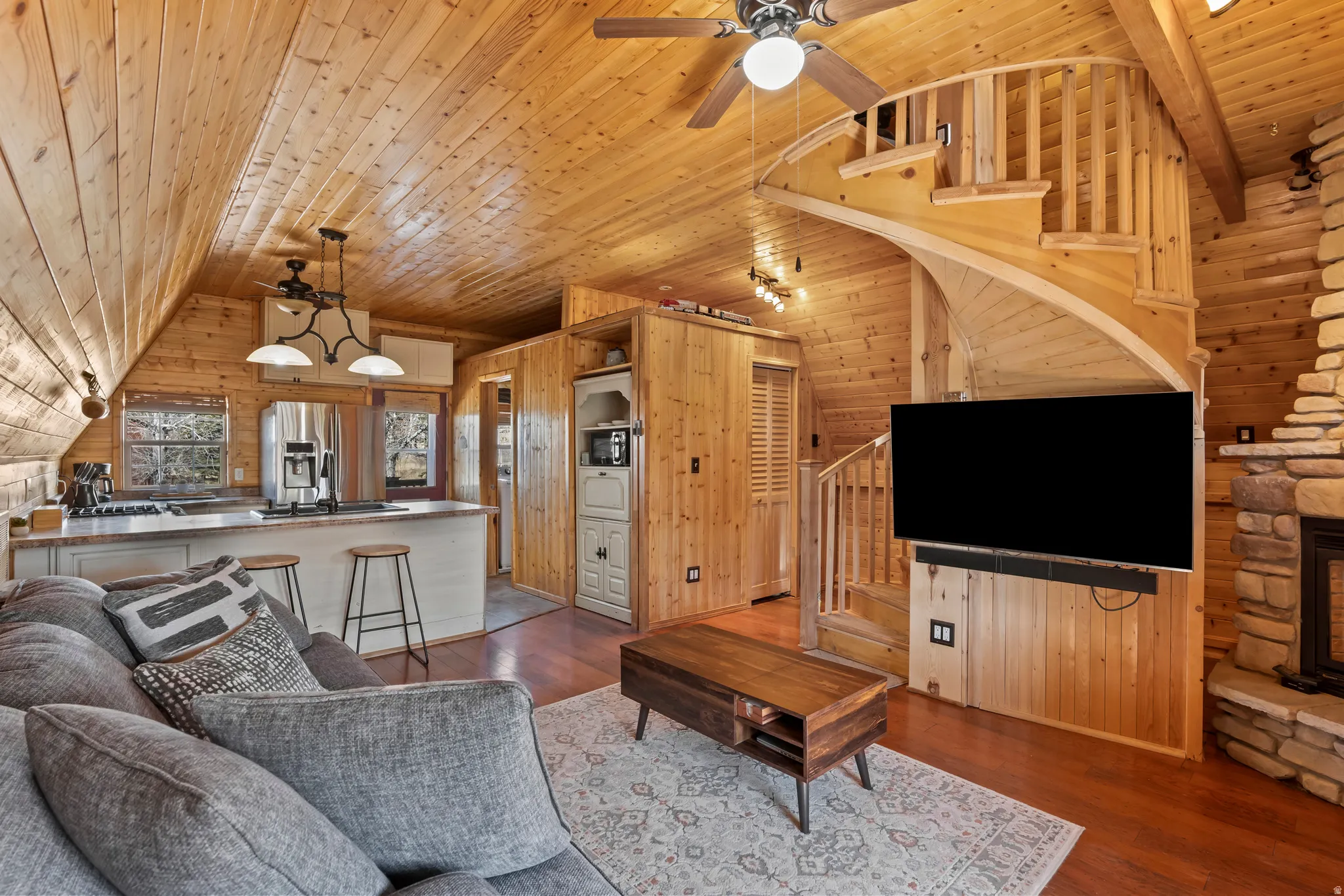 Living room with ceiling fan, a vaulted wood ceiling, wooden walls, and dark wood-type flooring