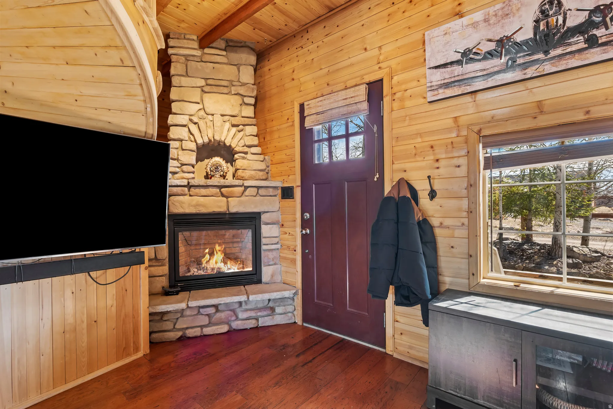 Entrance foyer featuring wooden walls, a wood ceiling with exposed beams, dark wood-style floors, a stone fireplace, and healthy amount of natural light