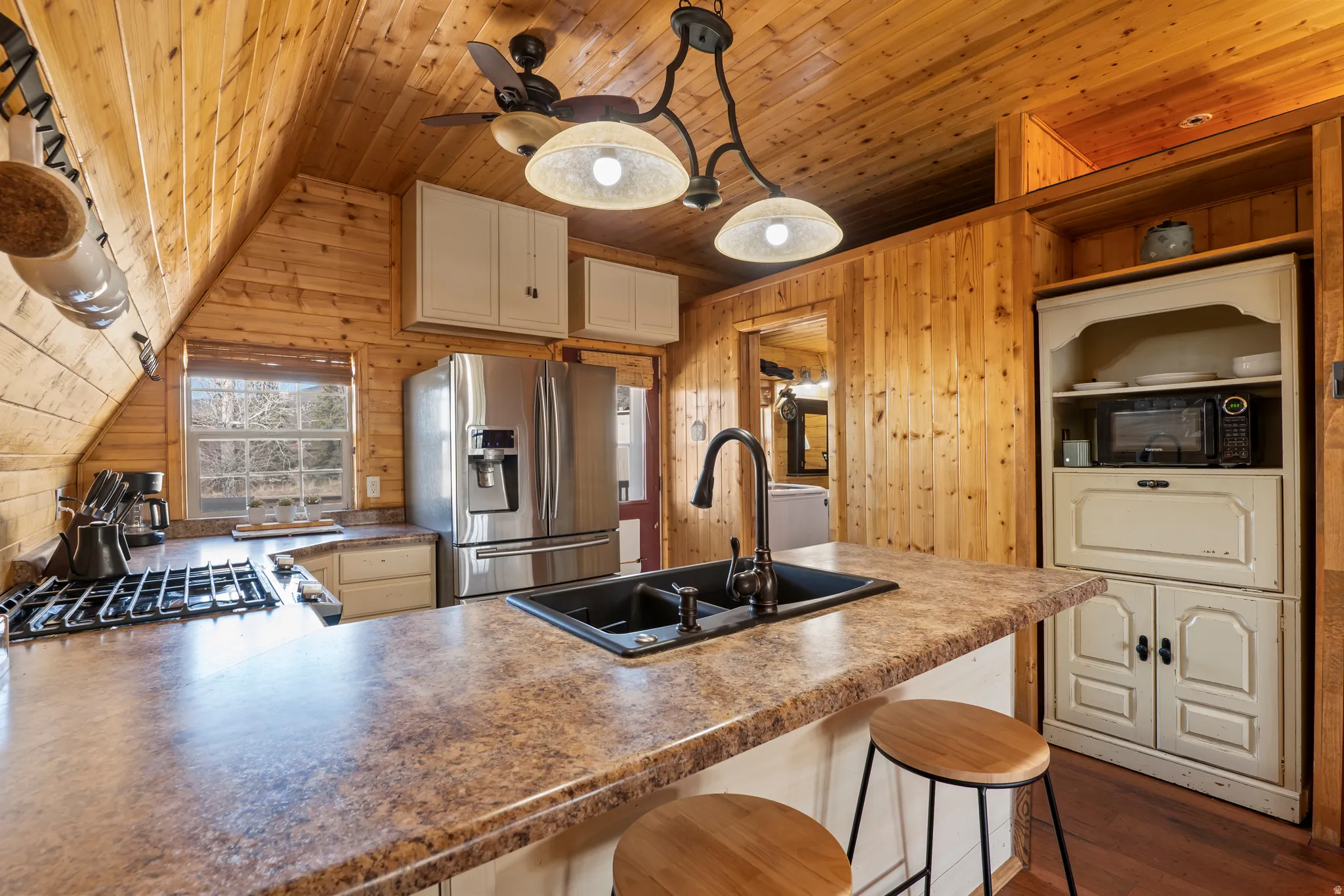 Kitchen with a peninsula, stainless steel fridge, a kitchen bar, a vaulted wood ceiling, and wood walls