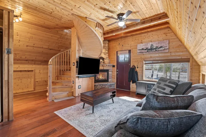 Living area with wood walls, a ceiling fan, wood-type flooring, a vaulted wooden ceiling, and a fireplace