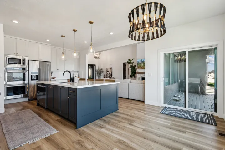 Kitchen with stainless steel appliances, suspended lighting, two tone color scheme, light wood-style floors, and an island with sink