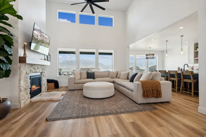 Living area featuring a fireplace, light wood-style flooring, ceiling fan, and a high ceiling