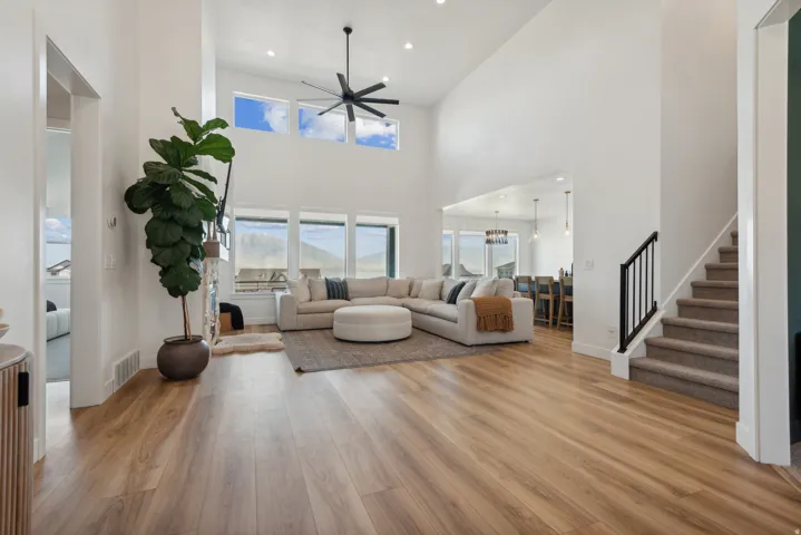 Living room with light wood-style flooring, a high ceiling, recessed lighting, and a ceiling fan