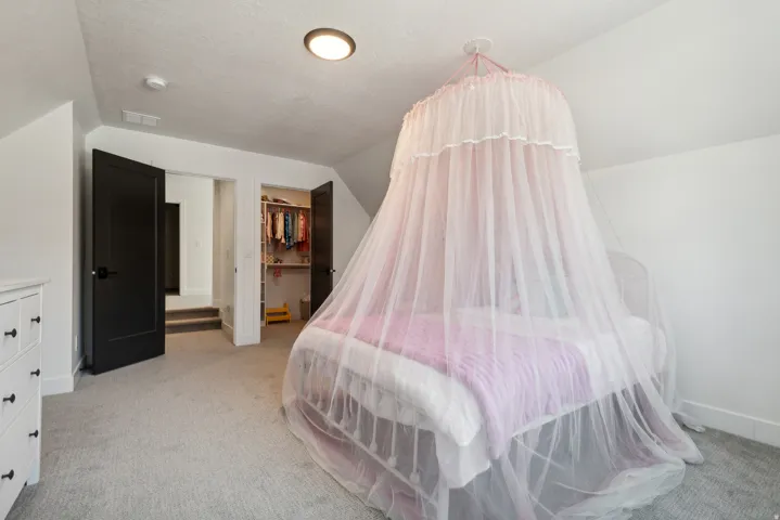 Bedroom with light carpet, a walk in closet, and vaulted ceiling