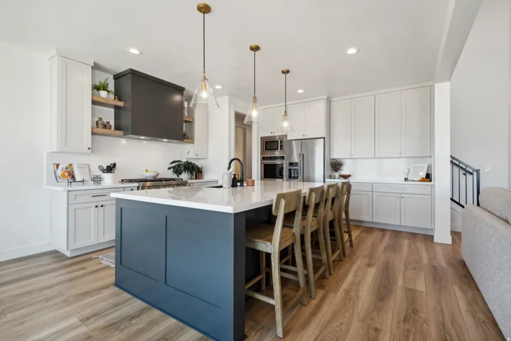 Two tone kitchen featuring dual tone cabinetry, light wood-style floors, a center island with sink, and backsplash