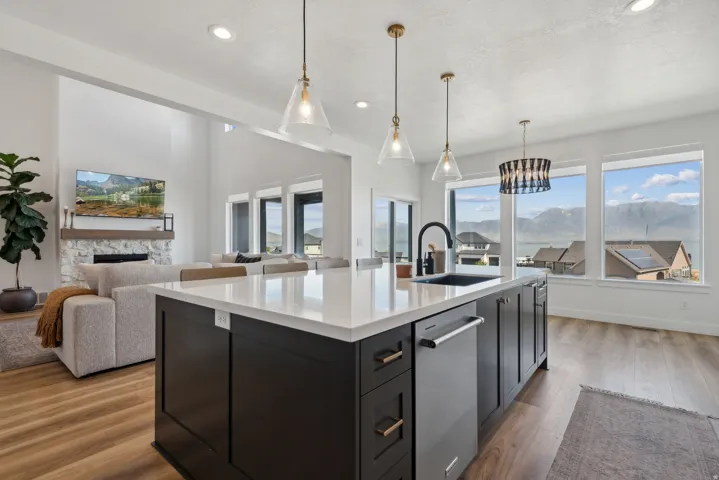 Kitchen with open floor plan, an island with sink, stainless steel dishwasher, a stone fireplace, and light wood-type flooring