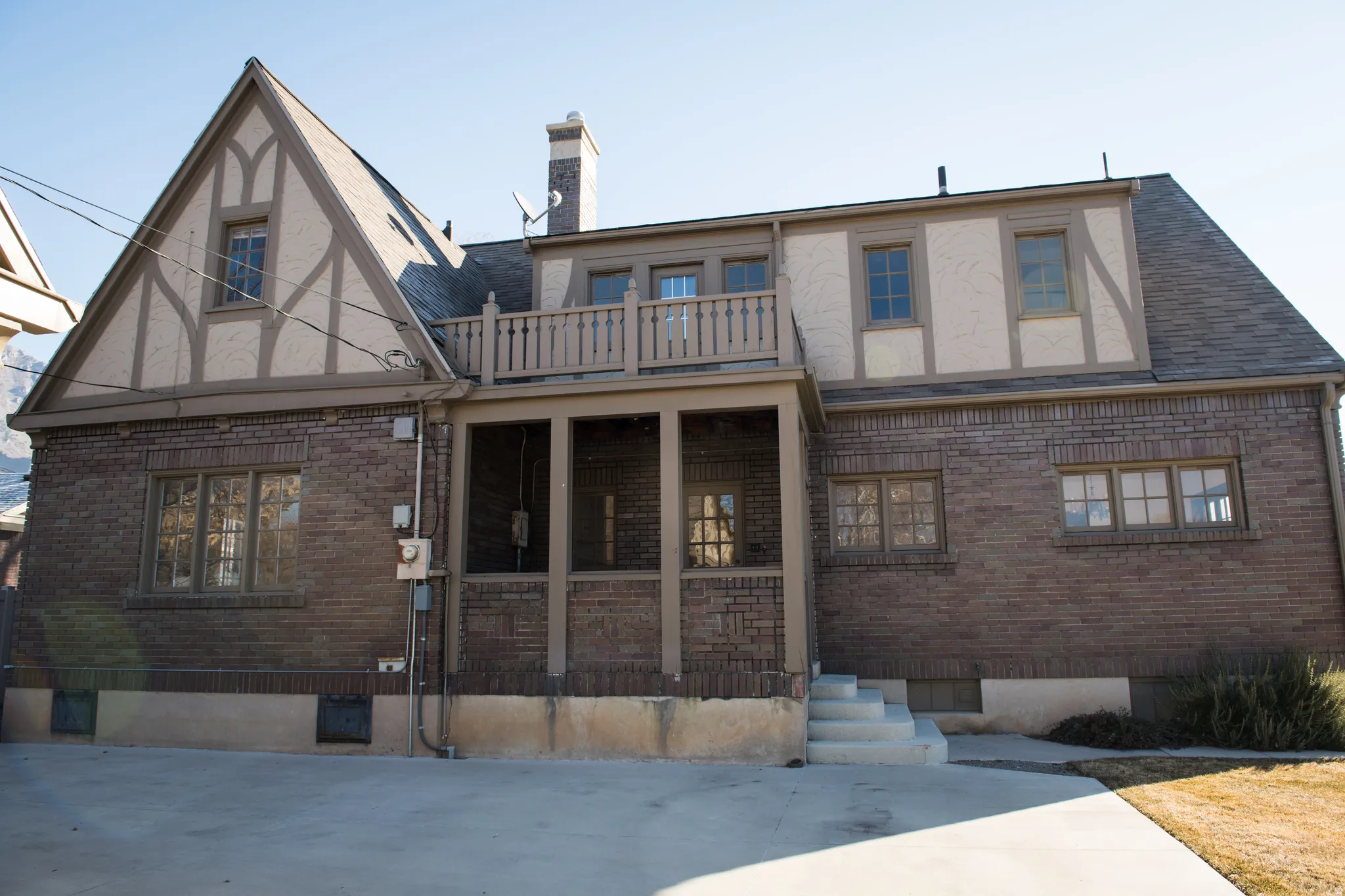 Rear view of house with brick siding, a balcony, stucco siding, and a chimney
