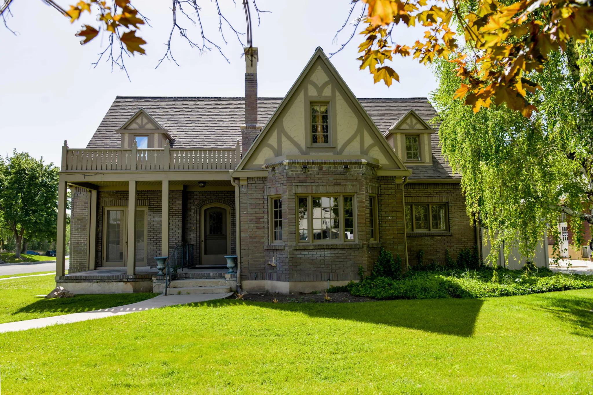 Tudor-style house featuring brick siding, a front yard, a chimney, and a shingled roof