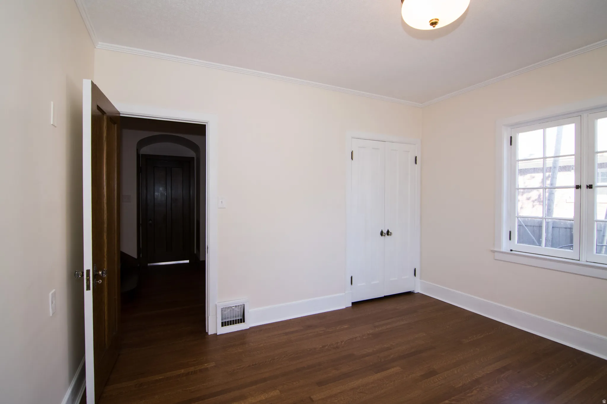 Unfurnished bedroom with dark wood-style floors, a closet, and ornamental molding