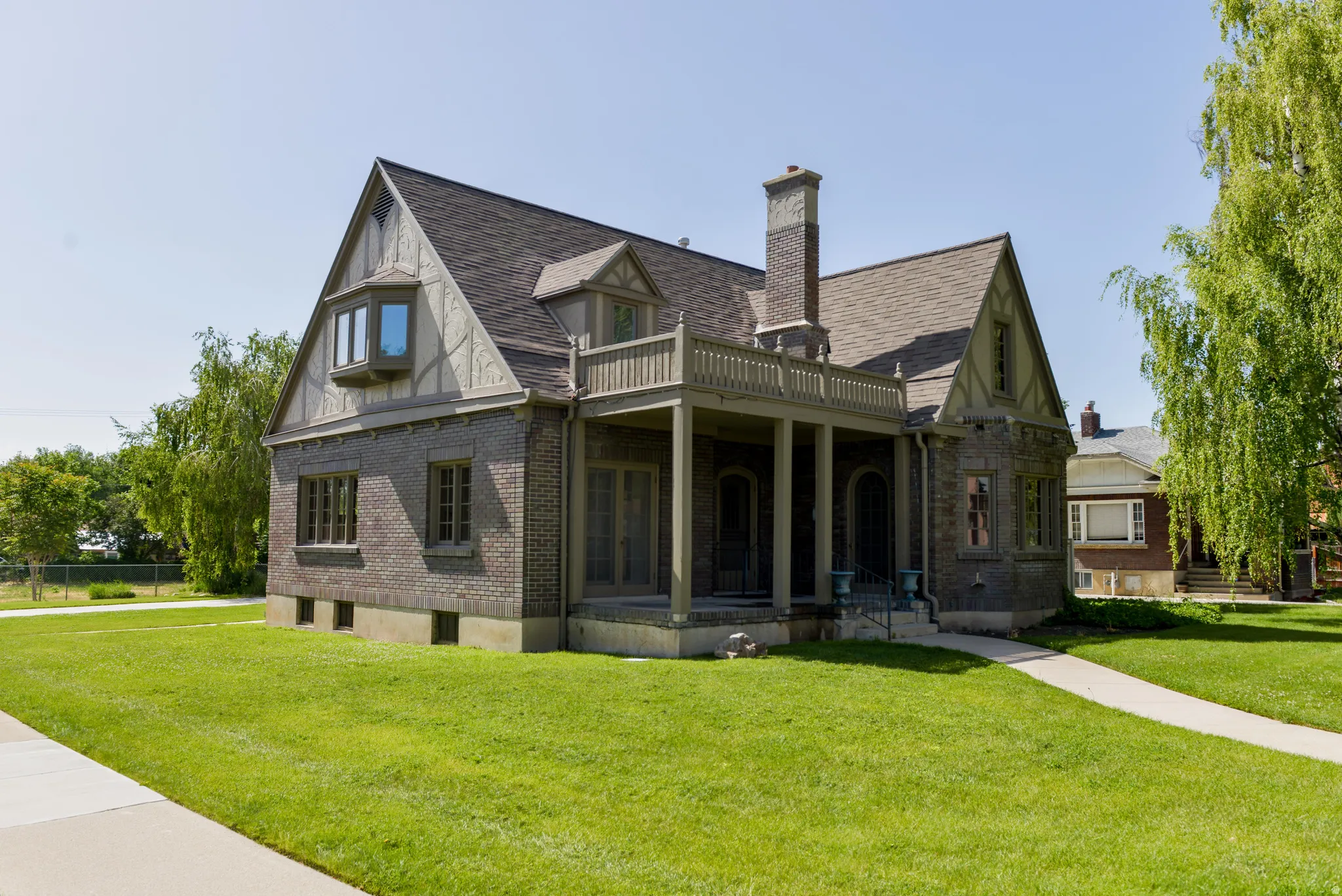 View of front facade featuring brick siding, a chimney, covered porch, and roof with shingles