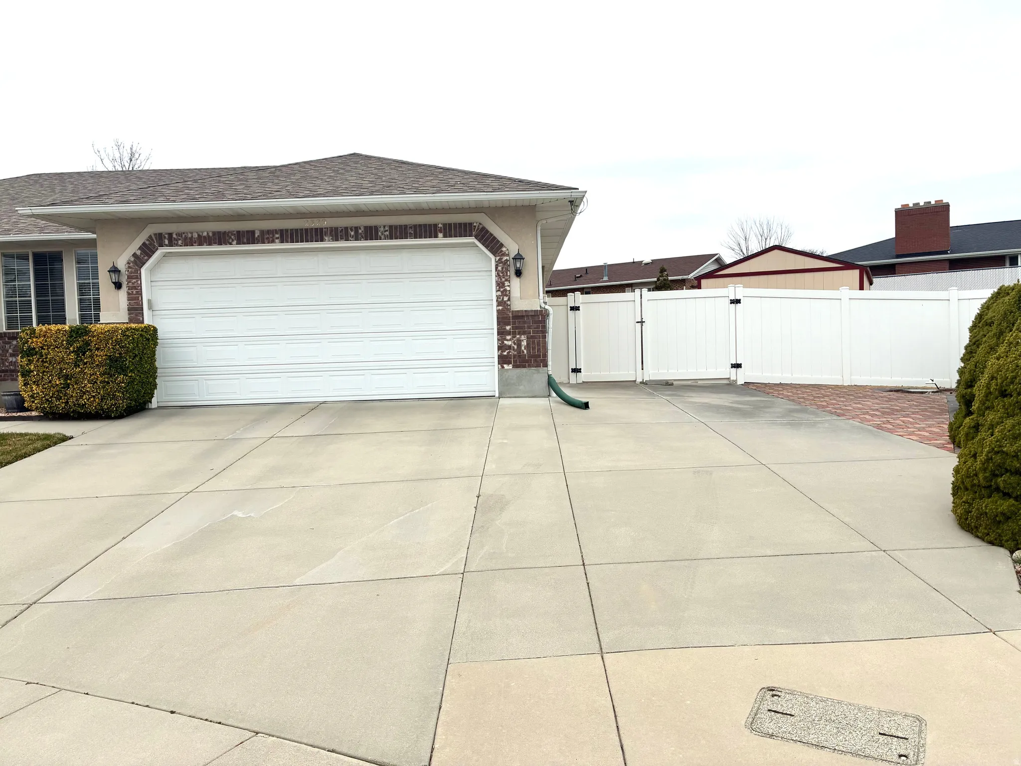 View of side of property featuring a gate, brick siding, a garage, driveway, and a shingled roof