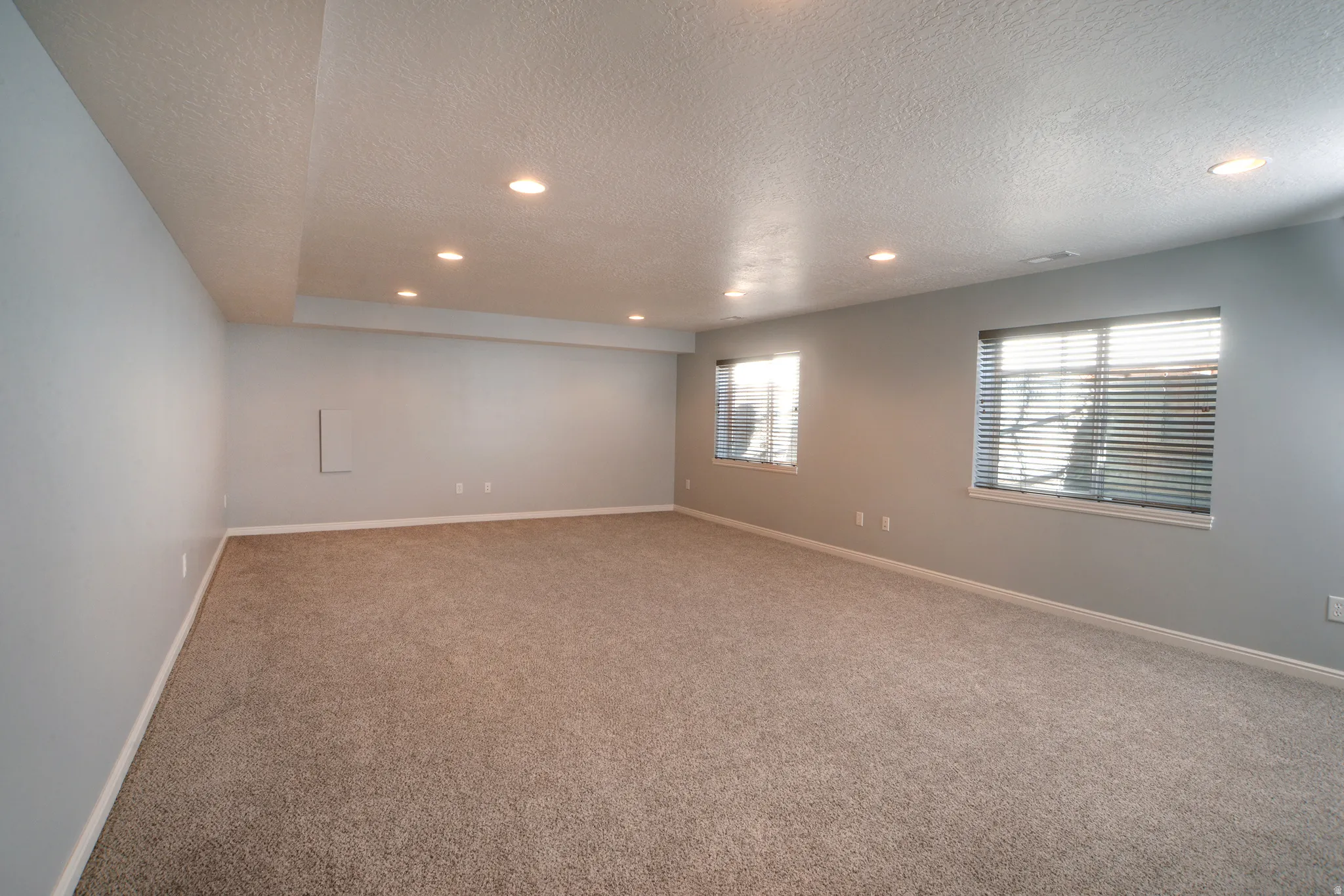 Carpeted empty room with a textured ceiling and recessed lighting