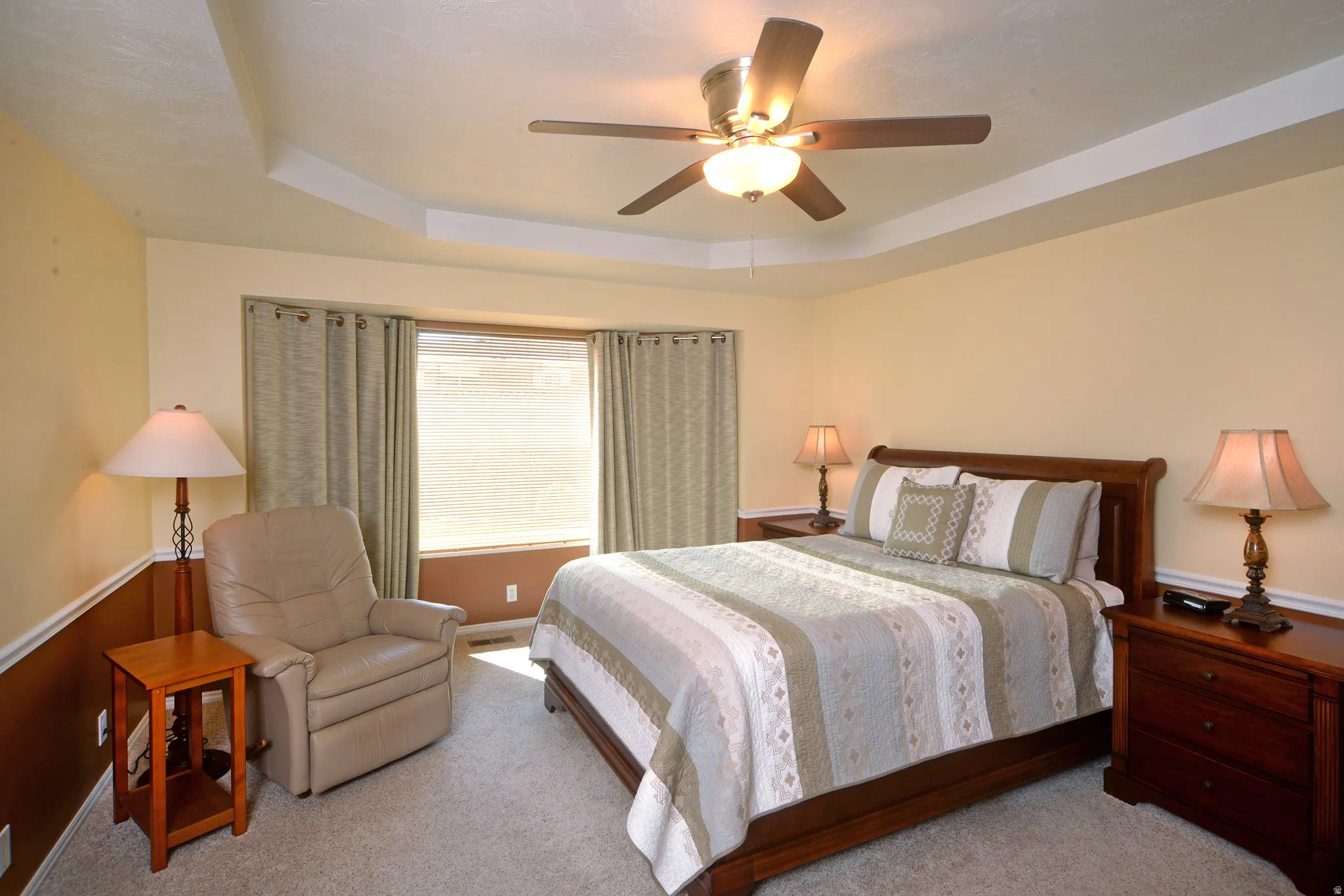 Carpeted bedroom with a tray ceiling and a ceiling fan