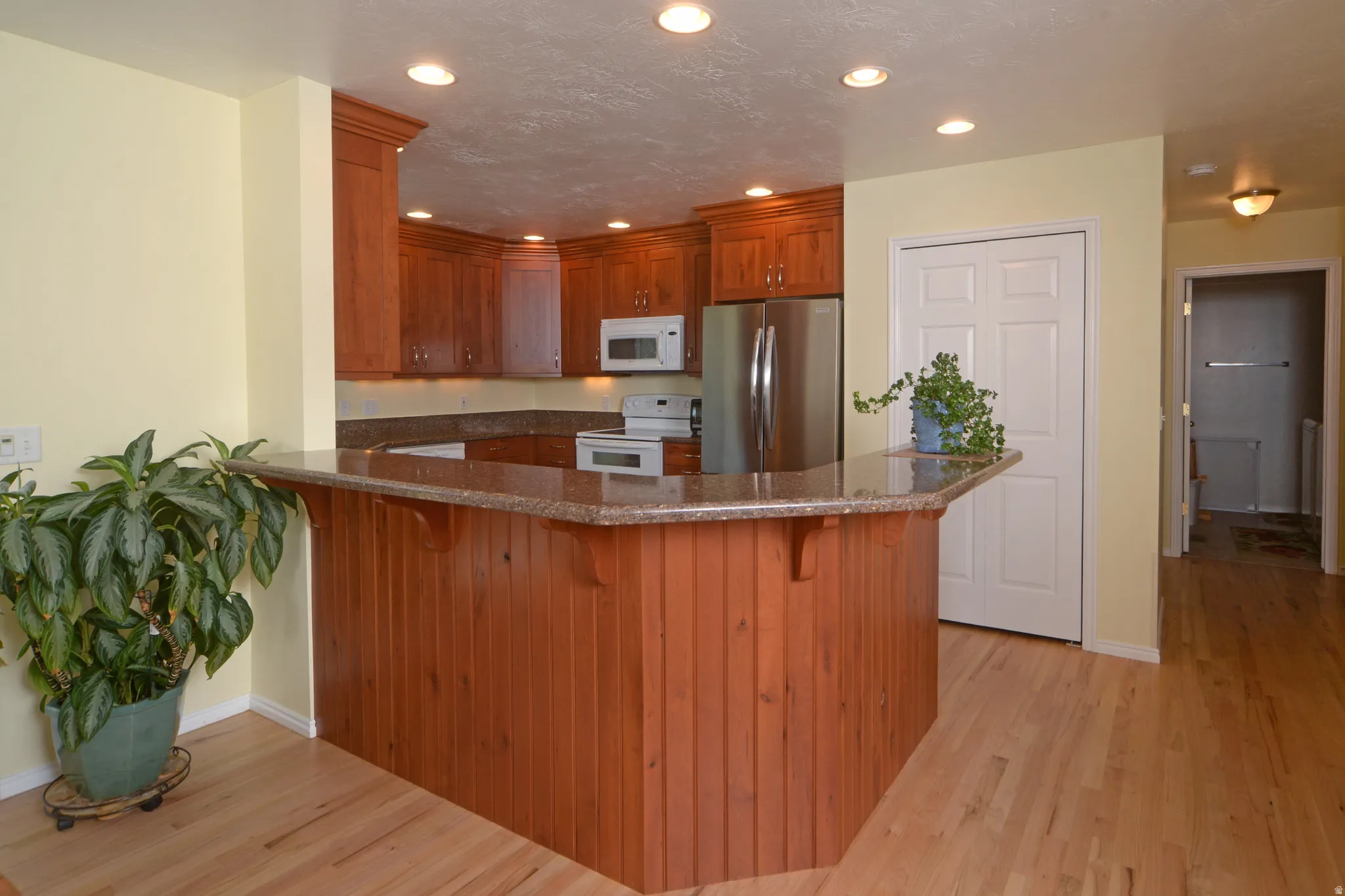 Kitchen featuring a peninsula, dark stone countertops, a kitchen bar, white appliances, and wood finish cabinets