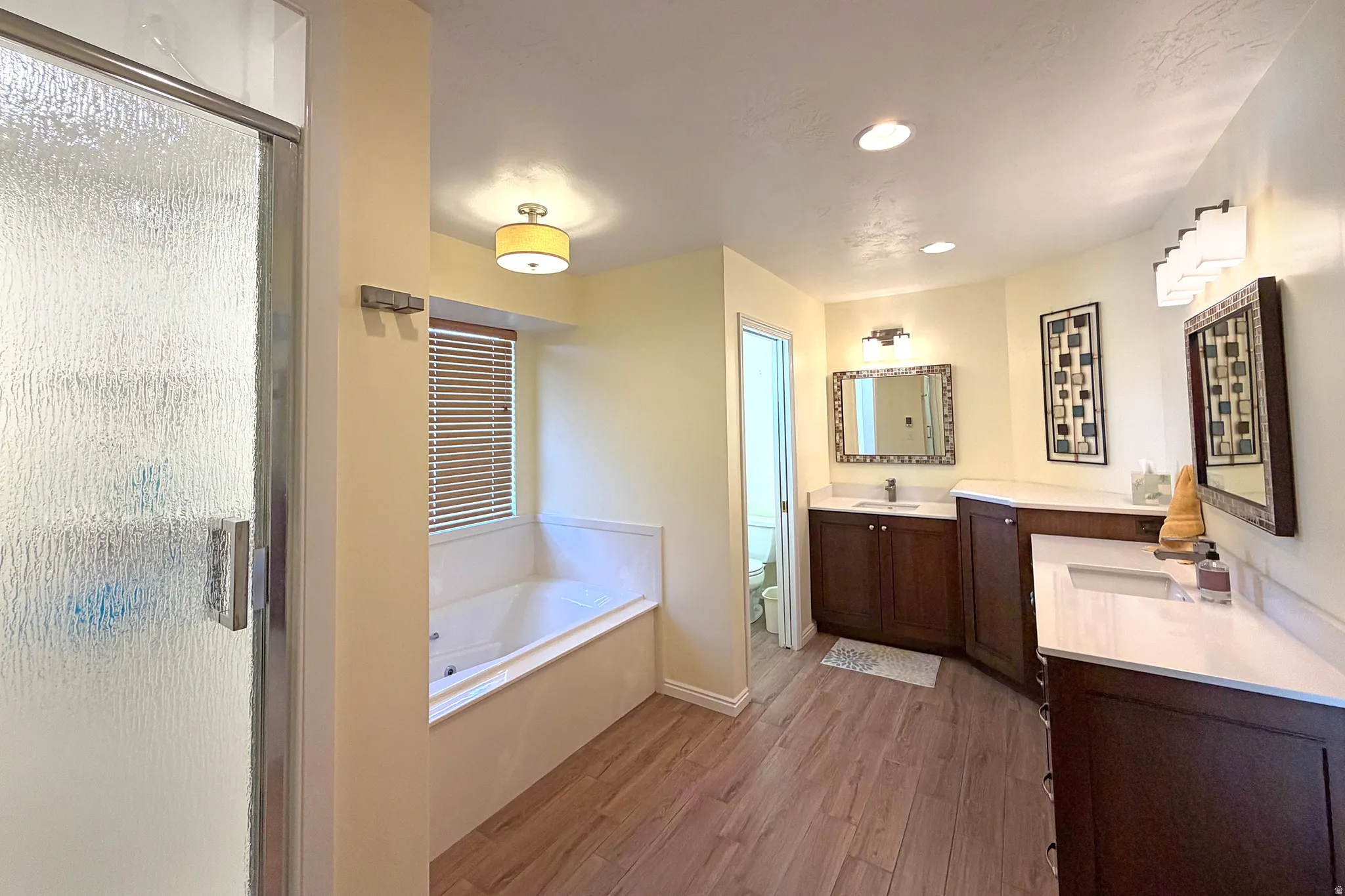 Bathroom featuring two vanities, light wood-type flooring, a shower stall, a bath, and recessed lighting