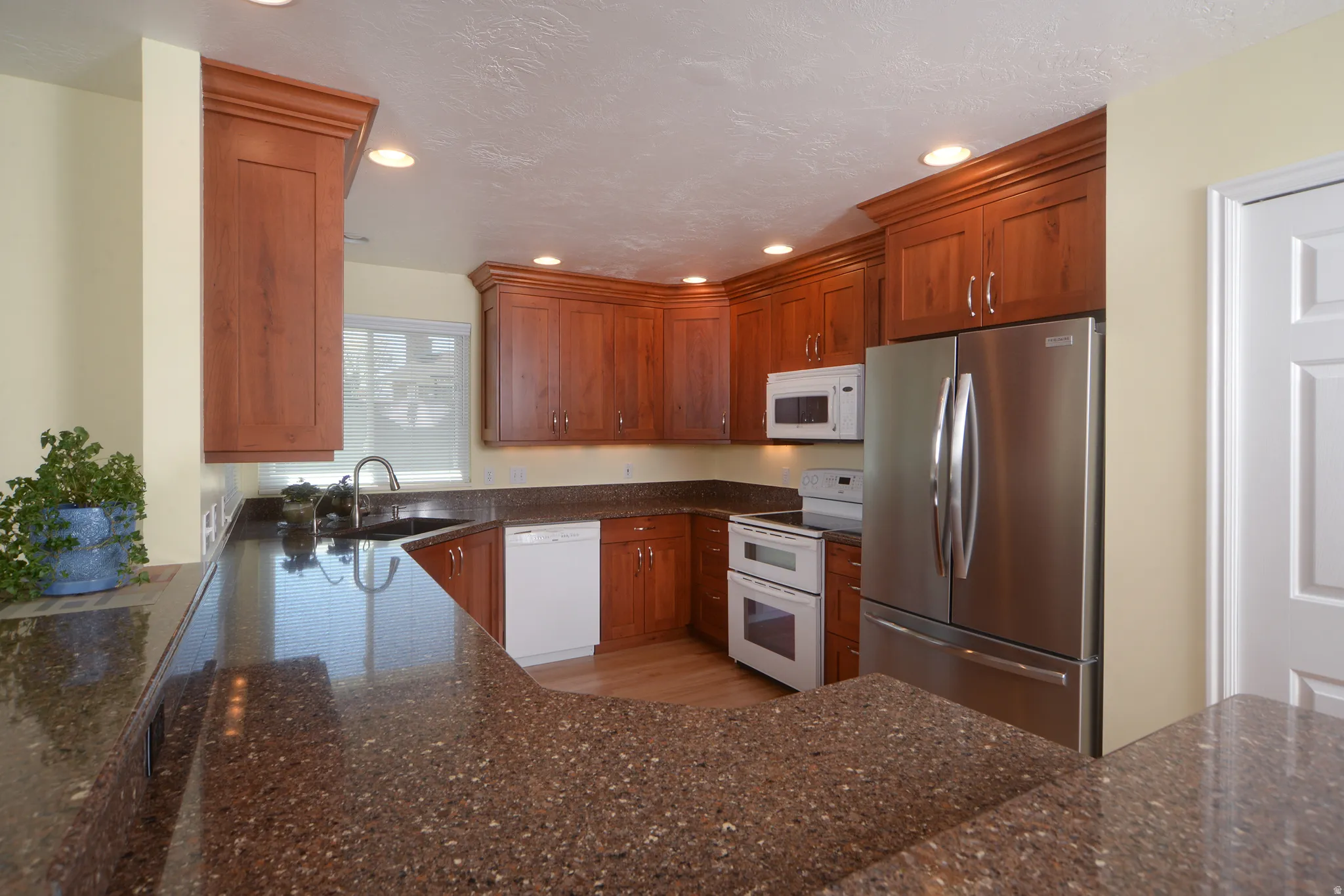 Kitchen with white appliances, dark stone counters, wood finish cabinets, and recessed lighting
