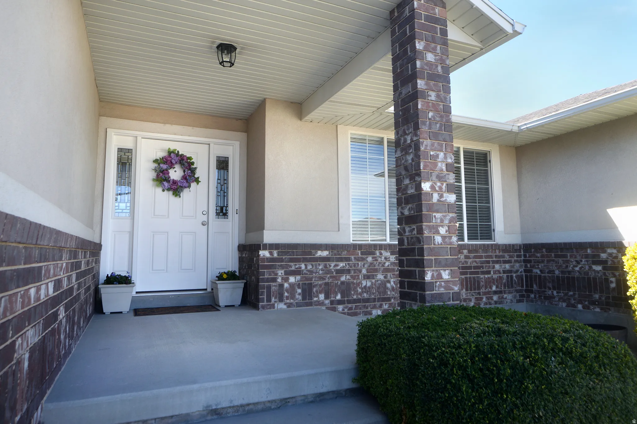 Doorway to property with covered porch, stucco siding, and brick siding
