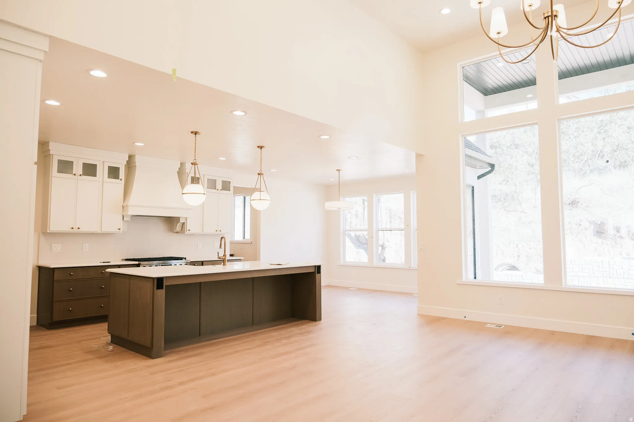 Open-concept kitchen and living area featuring high vaulted ceilings, large windows, wood-finish flooring, a spacious kitchen island with an integrated sink, and recessed lighting throughout