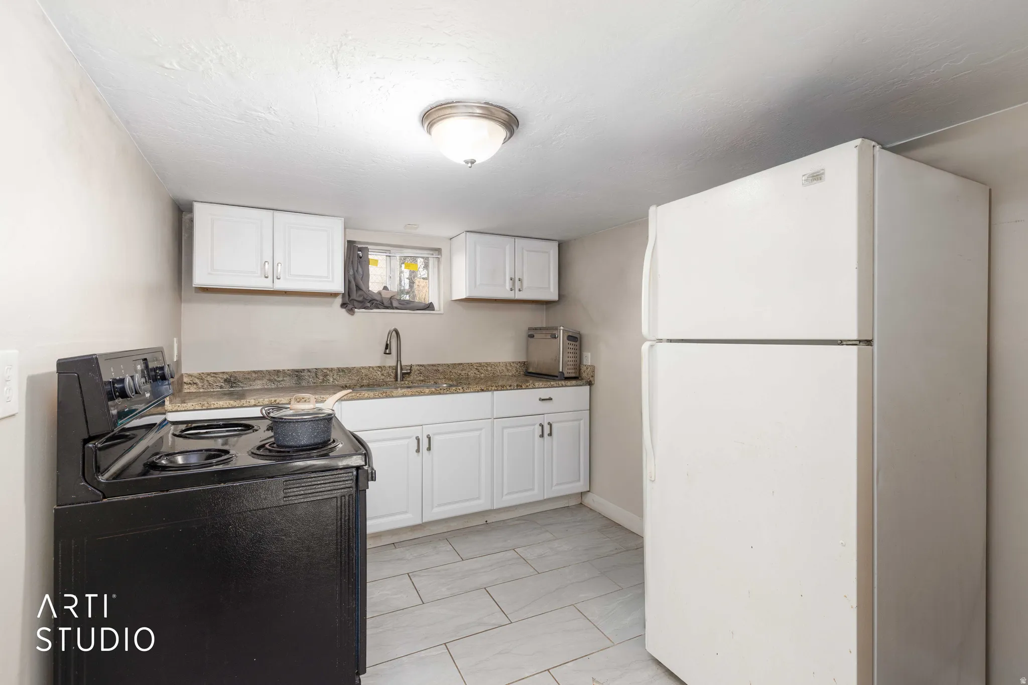 Kitchen with freestanding refrigerator, black / electric stove, and white cabinets