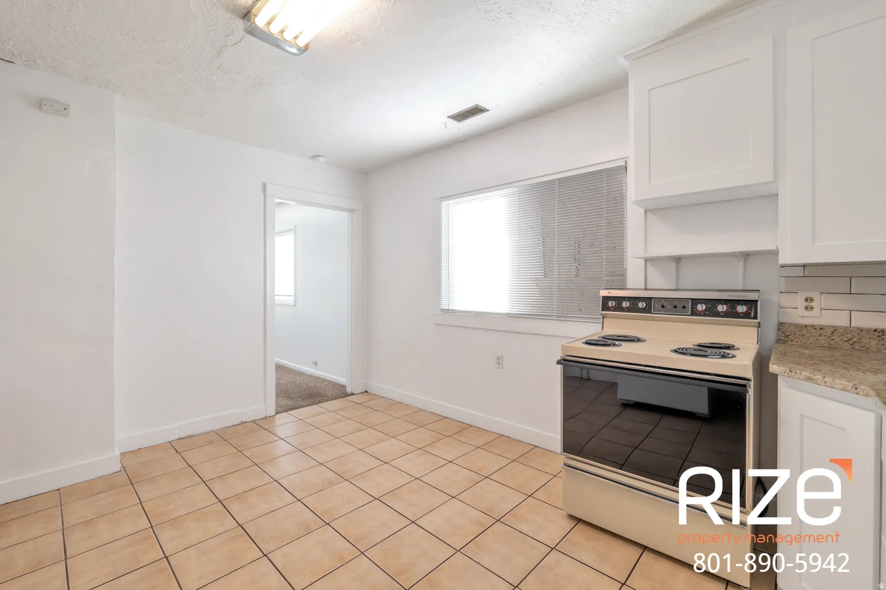 Kitchen with electric stove, light tile patterned floors, white cabinetry, and a textured ceiling