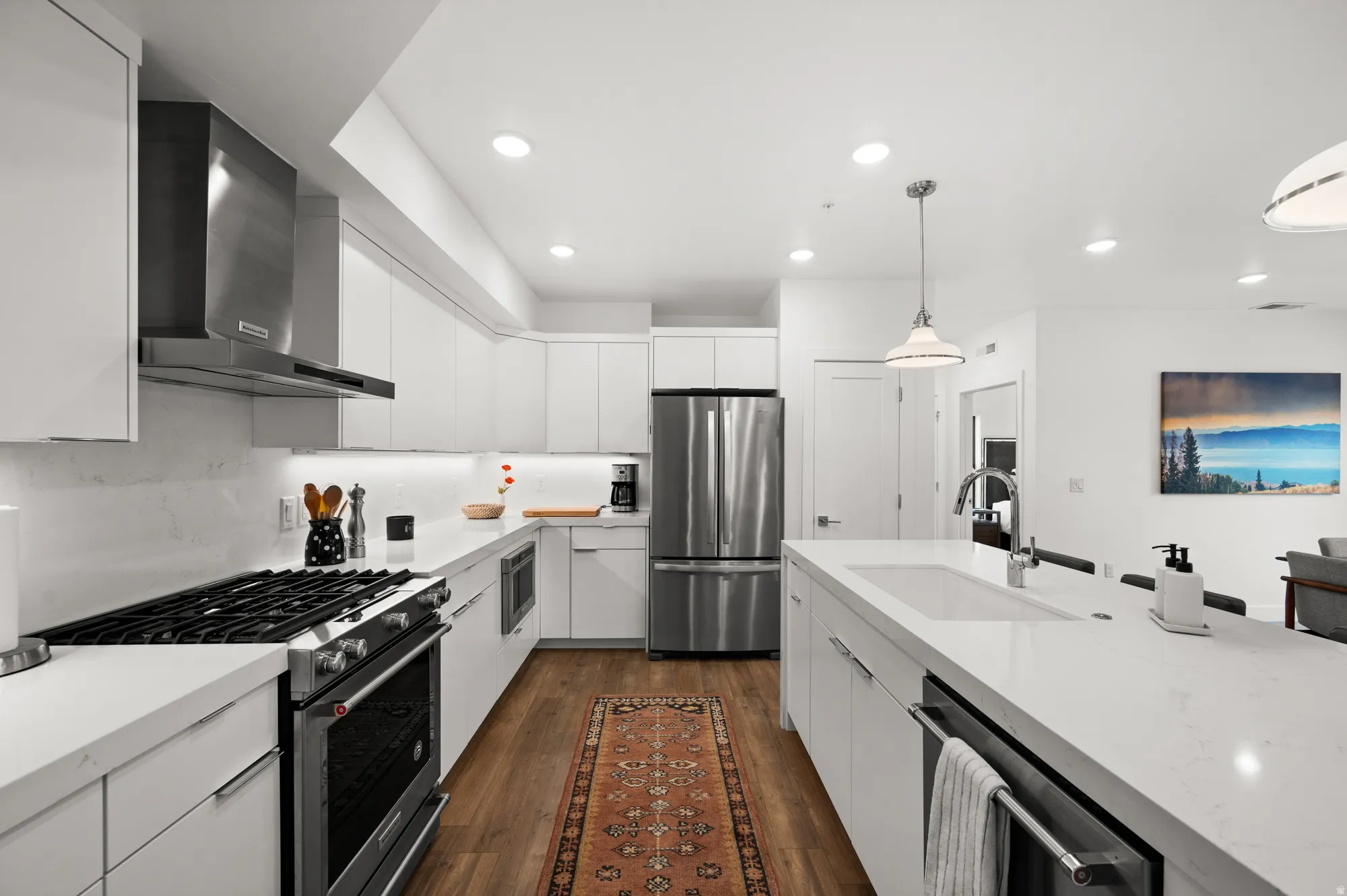 Kitchen with white cabinets, stainless steel appliances, dark wood-style flooring, hanging light fixtures, and light stone counters