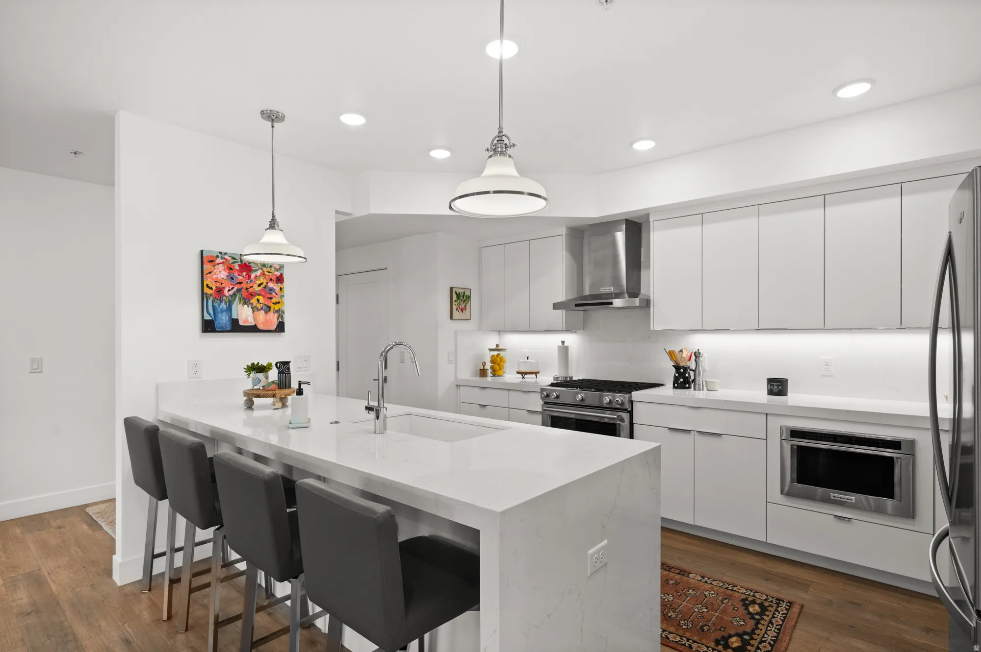 Kitchen with a peninsula, a breakfast bar area, white cabinets, light stone counters, and dark wood-type flooring