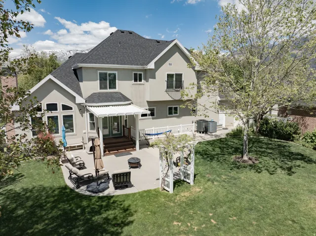 Expansive backyard featuring a concrete patio, covered deck, and manicured lawn