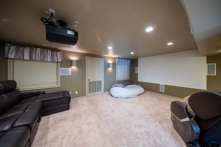 Dedicated media room featuring a ceiling-mounted projector, large projection screen, recessed lighting, wall sconces, and neutral-toned carpeting