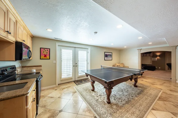 Lower-level recreational space featuring a compact kitchen with wood cabinetry, granite-finish countertops, and black appliances