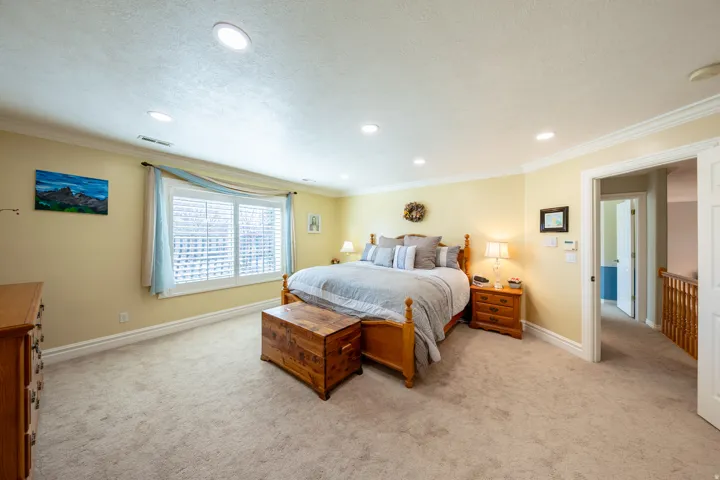 Spacious room featuring neutral carpeting, recessed lighting, crown molding, and a substantial window with plantation shutters