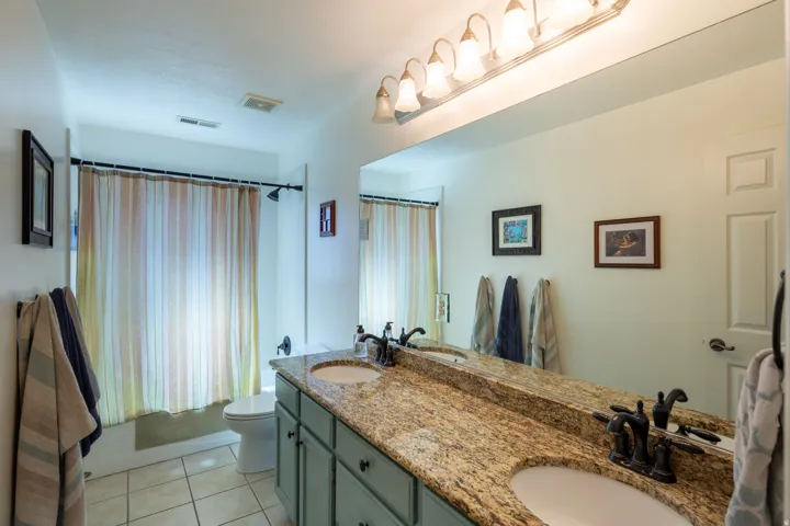 Bathroom featuring a double vanity with granite countertop, integrated sinks, and bronze-finish fixtures