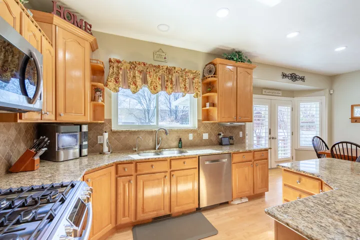 Kitchen featuring light wood cabinetry, granite-finish countertops, and a tile backsplash