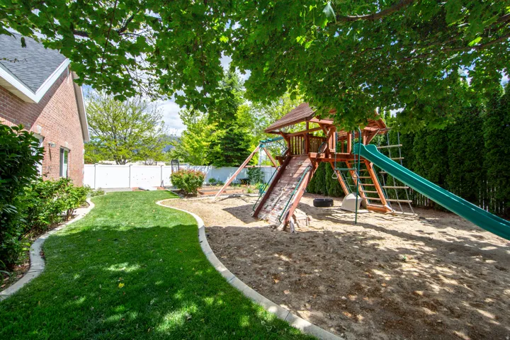 Expansive backyard featuring a lush lawn, mature trees, and a dedicated sand play area