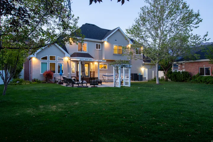 Expansive backyard featuring a large paved patio, pergola, and manicured lawn