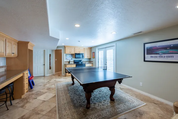 Spacious lower-level area featuring a full kitchen with light wood cabinetry, a built-in bar, and tile flooring