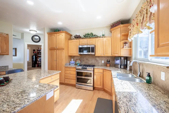 Bright kitchen featuring light wood cabinetry, stone countertops, stainless steel appliances, wood-finish flooring, and recessed lighting