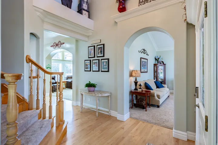 Entryway featuring light wood-finish flooring, a carpeted staircase with wood banister, and arched doorways