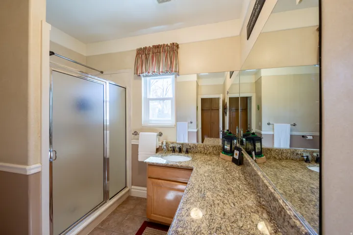 Bathroom featuring a dual vanity with a granite-finish countertop, two undermount sinks, and a framed mirror