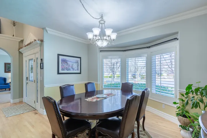 Dining area featuring a bay window with plantation shutters, crown molding, a decorative chandelier, and wood-finish flooring