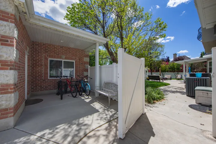 Covered patio area featuring brick siding with stone accents, a white vinyl fence, and a concrete surface