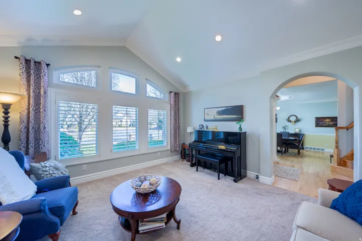 Vaulted ceiling with recessed lighting, large windows with plantation shutters and arched transoms, plush carpeting, and an arched entryway to an adjacent room