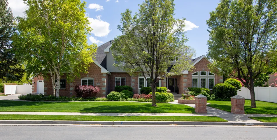Brick facade residence featuring a multi-gabled roof, mature landscaping, a curved paver walkway, a decorative fountain, and a two-car garage