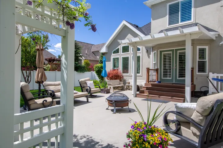 Expansive concrete patio featuring a white pergola, multi-level wood deck, and a stucco exterior with multiple windows