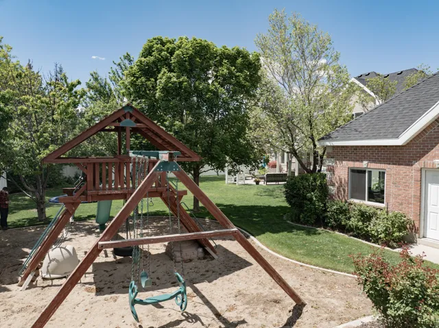 Backyard featuring a wooden playset with swings and a slide, a sandy play area, and a manicured lawn