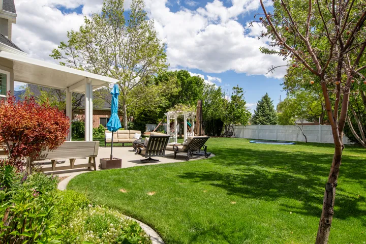 Expansive backyard featuring a large green lawn, a white pergola structure, and a patio area with a covered extension