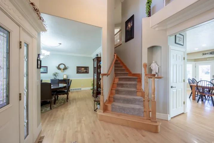Foyer featuring light wood-finish flooring, a carpeted staircase with wood banister and balusters, and a recessed wall niche