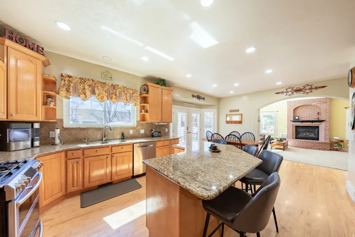 Spacious kitchen featuring light wood cabinetry, stone countertops, stainless steel appliances, and recessed lighting