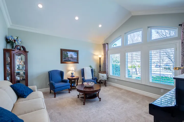 Living area featuring vaulted ceilings, recessed lighting, carpet flooring, a large window array with plantation shutters, and crown molding