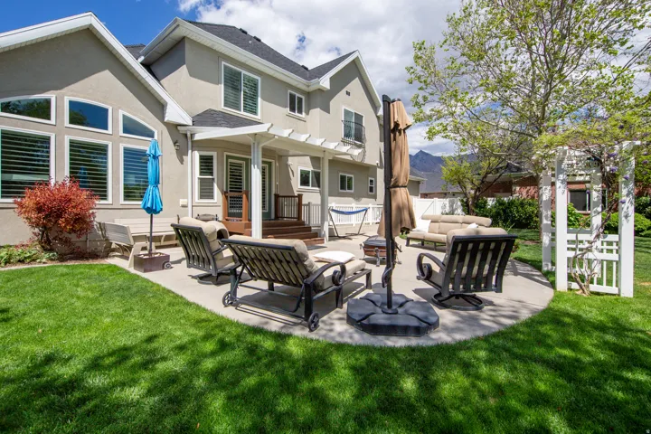 Spacious backyard featuring a curved concrete patio, a pergola-covered deck, a white wooden arbor, and a substantial stucco exterior